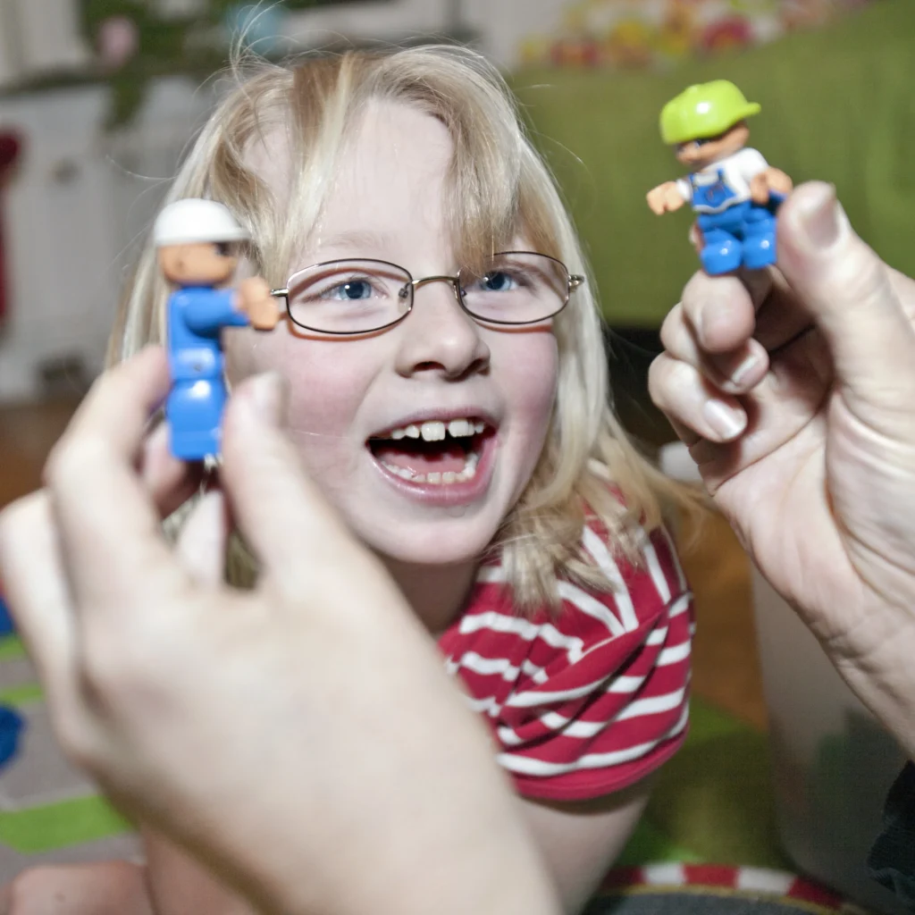 Bild på Elmie som ler stort och mammas händer som håller i Duplogubbar